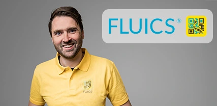 A smiling man wearing a yellow polo shirt with the logo "FLUICS" on it. The background is gray, and there is a QR code next to the logo.