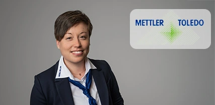 A smiling professional woman in business attire with a blue tie, posed against a gray background. The image includes the METTLER TOLEDO logo in the top right corner.