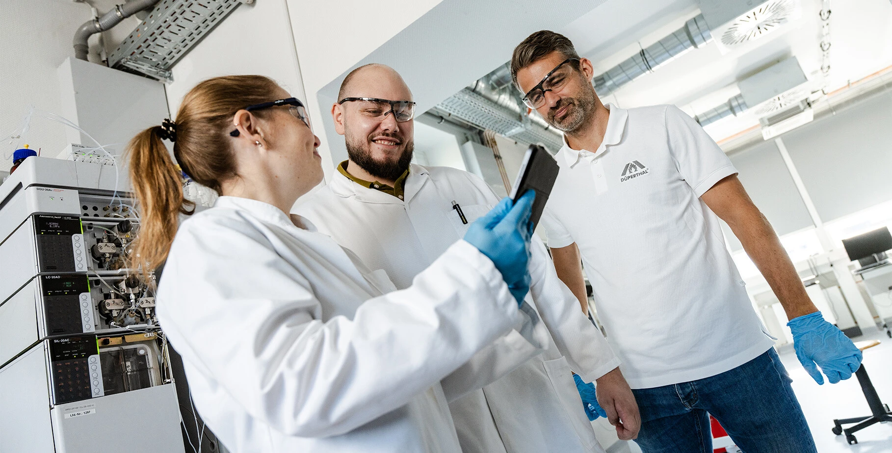 Drei Personen in einem Labor, die auf ein Tablet schauen