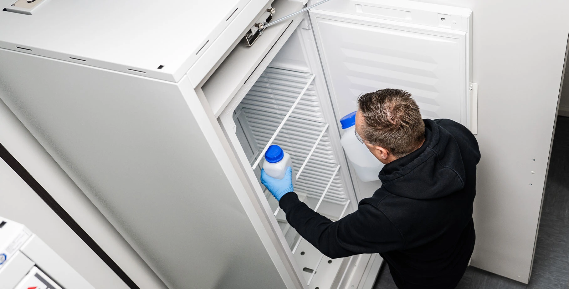 Ein Mann mit Handschuhen hält einen Behälter in einer leeren Kühlschranktür.