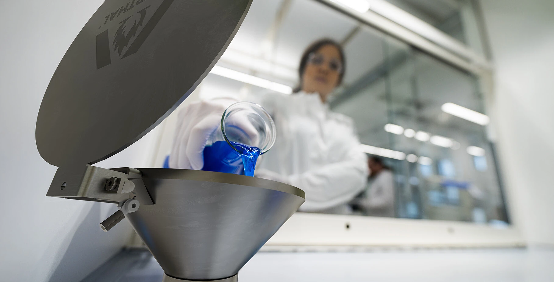 Eine Wissenschaftlerin gießt eine blaue Flüssigkeit aus einem Glasbehälter in einen Metalltrichter.