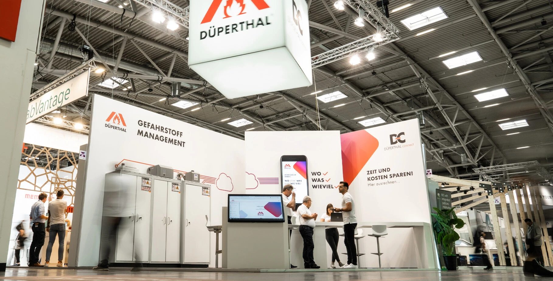 Exhibition booth featuring DÜPERTHAL branding, showcasing safety management products with staff interacting and a large digital display.