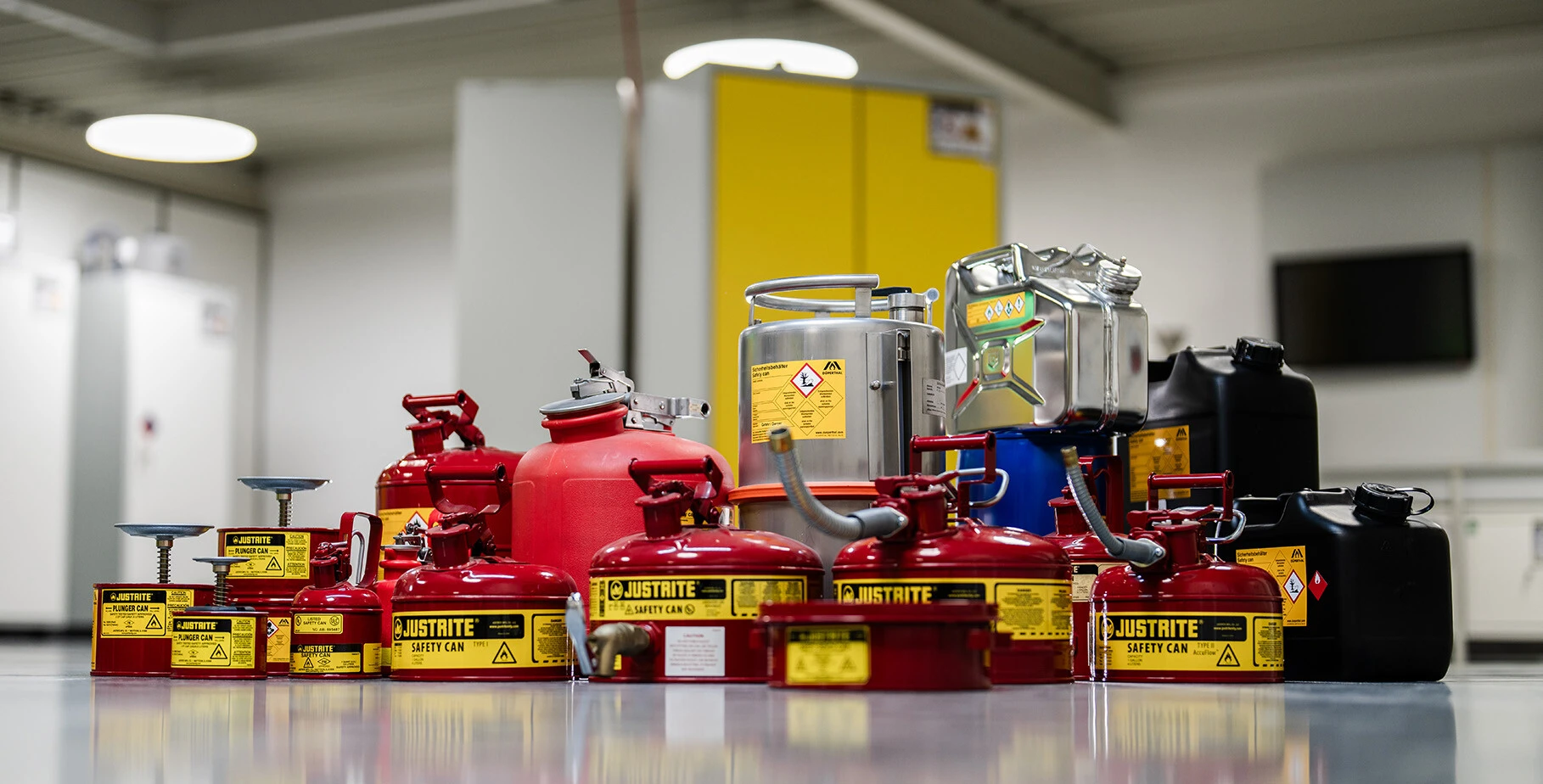 A collection of various fuel safety cans, including red and black containers, on a clean floor in a well-lit room.