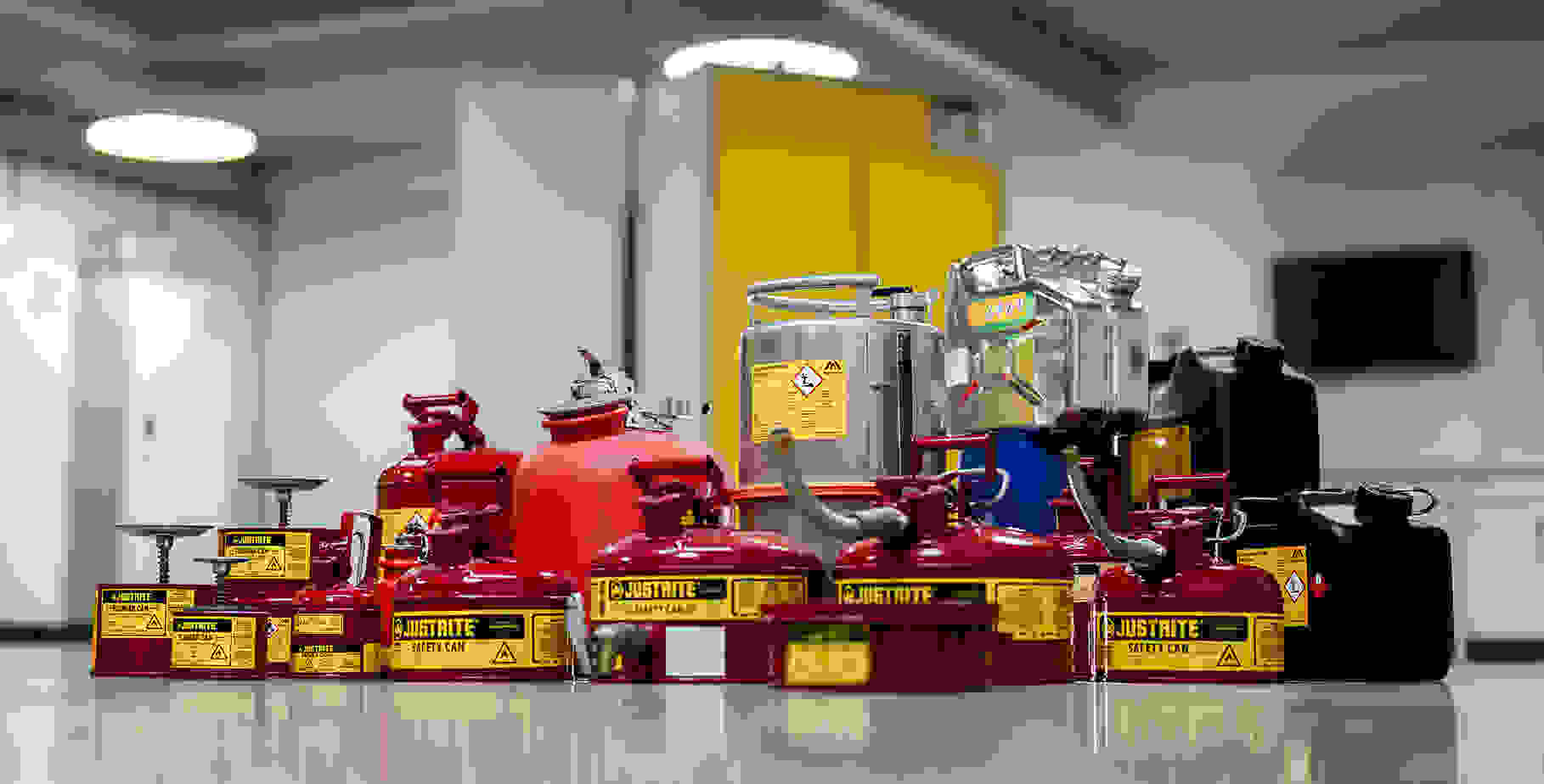 A collection of various fuel safety cans, including red and black containers, on a clean floor in a well-lit room.