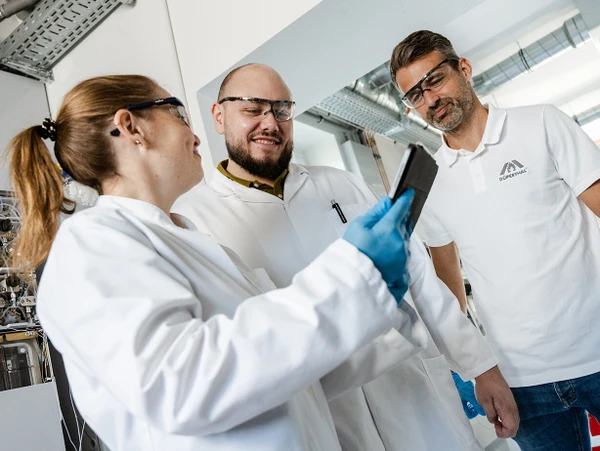 Drei Personen in einem Labor, die auf ein Tablet schauen