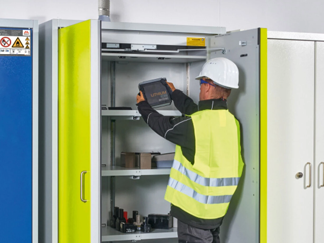 Arbeiter in Schutzausrüstung greift nach einem Behälter in einem geöffneten Aufbewahrungsschrank.