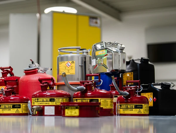 A collection of various fuel safety cans, including red and black containers, on a clean floor in a well-lit room.