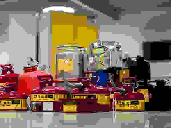 A collection of various fuel safety cans, including red and black containers, on a clean floor in a well-lit room.