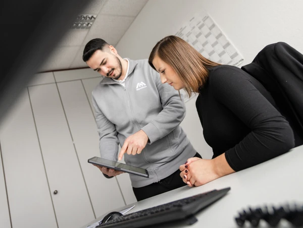 Ein Mann zeigt einer Frau auf einem Tablet Informationen am Schreibtisch