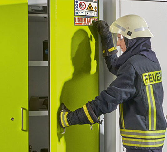 Feuerwehrmann öffnet einen grünen Schrank für Lithiumbatterien.