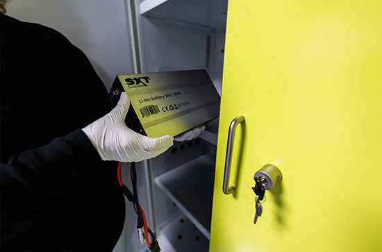 Eine Person mit Handschuhen hält eine Lithium-Batterie in der Nähe eines gelben Schranks.