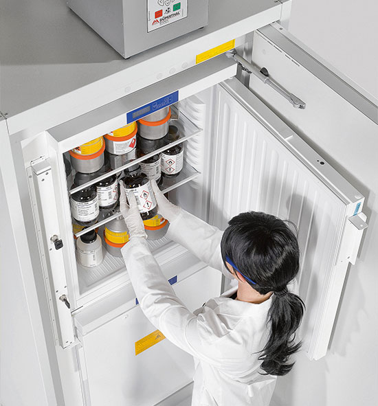 Laborant in einem weißen Laborkittel entnimmt Chemikalien aus einem Kühlschrank für gefährliche Stoffe.