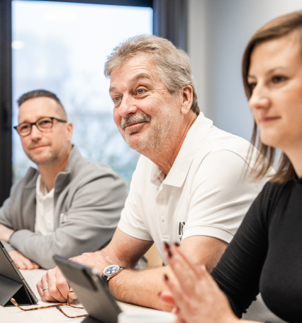 Trois personnes sont assises &agrave; une table et discutent. Il y a des tablettes devant elles. L'arri&egrave;re-plan est clair et accueillant.