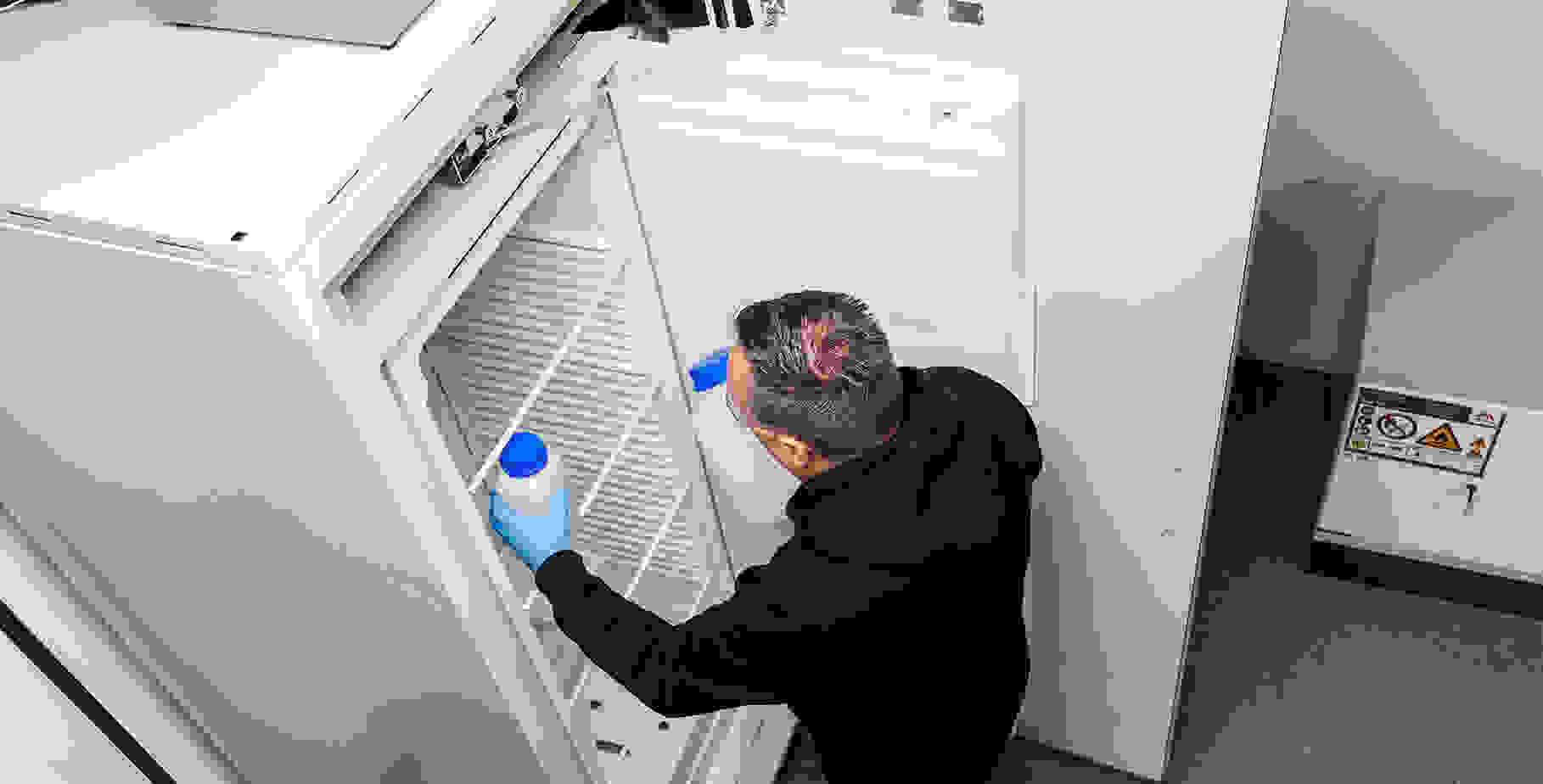 Un homme en sweat à capuche noir, portant des lunettes de protection, qui place une bouteille dans un congélateur.