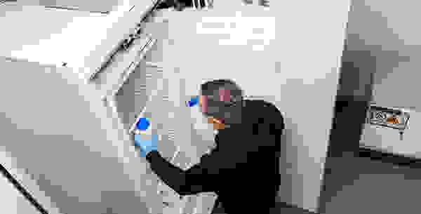 Un homme en sweat à capuche noir, portant des lunettes de protection, qui place une bouteille dans un congélateur.