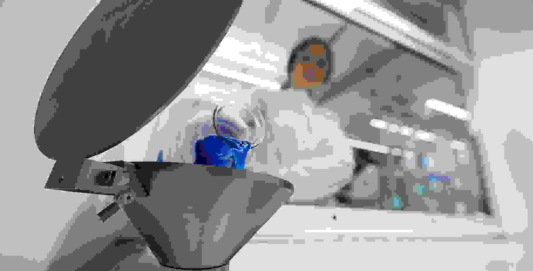 Une scientifique verse un liquide bleu d'un récipient en verre dans un Entonnoirs métallique.