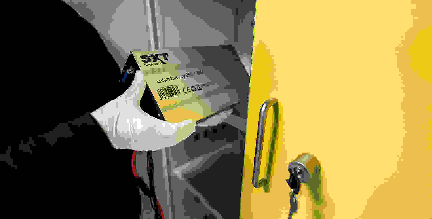 Une personne portant des gants blancs tient un accumulateur lithium-ion et le place dans une armoire jaune.