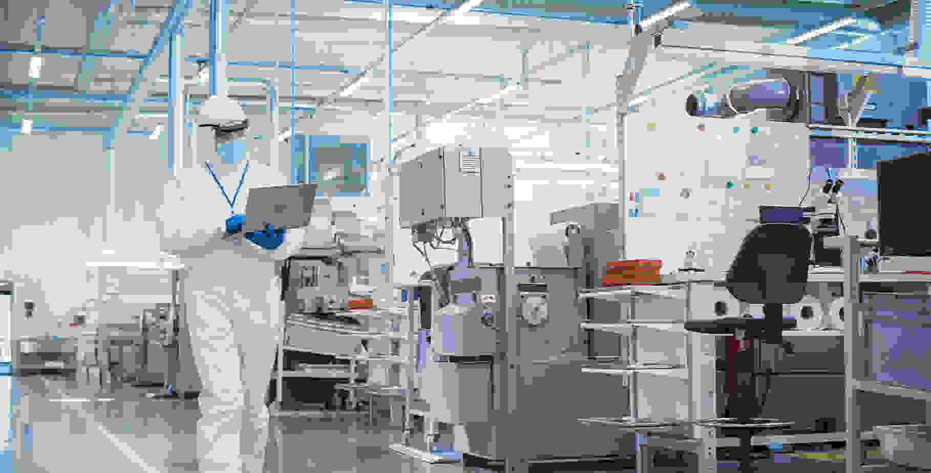 Un employé de laboratoire en tenue de protection travaille sur un ordinateur portable dans un laboratoire moderne équipé d'appareils techniques.