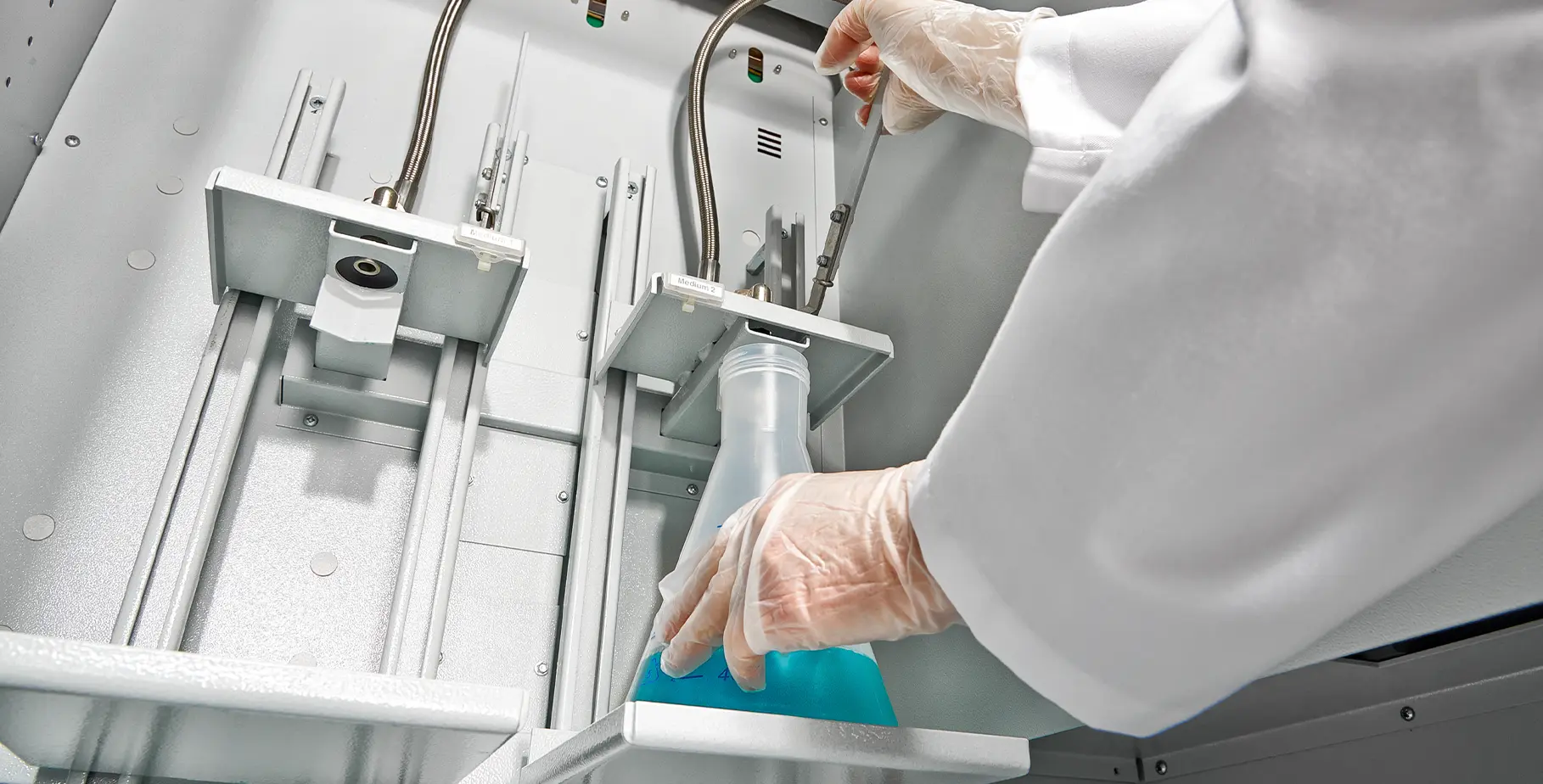 Un technicien de laboratoire tient un flacon Erlenmeyer contenant un liquide bleu dans un appareil comportant plusieurs tuyaux.