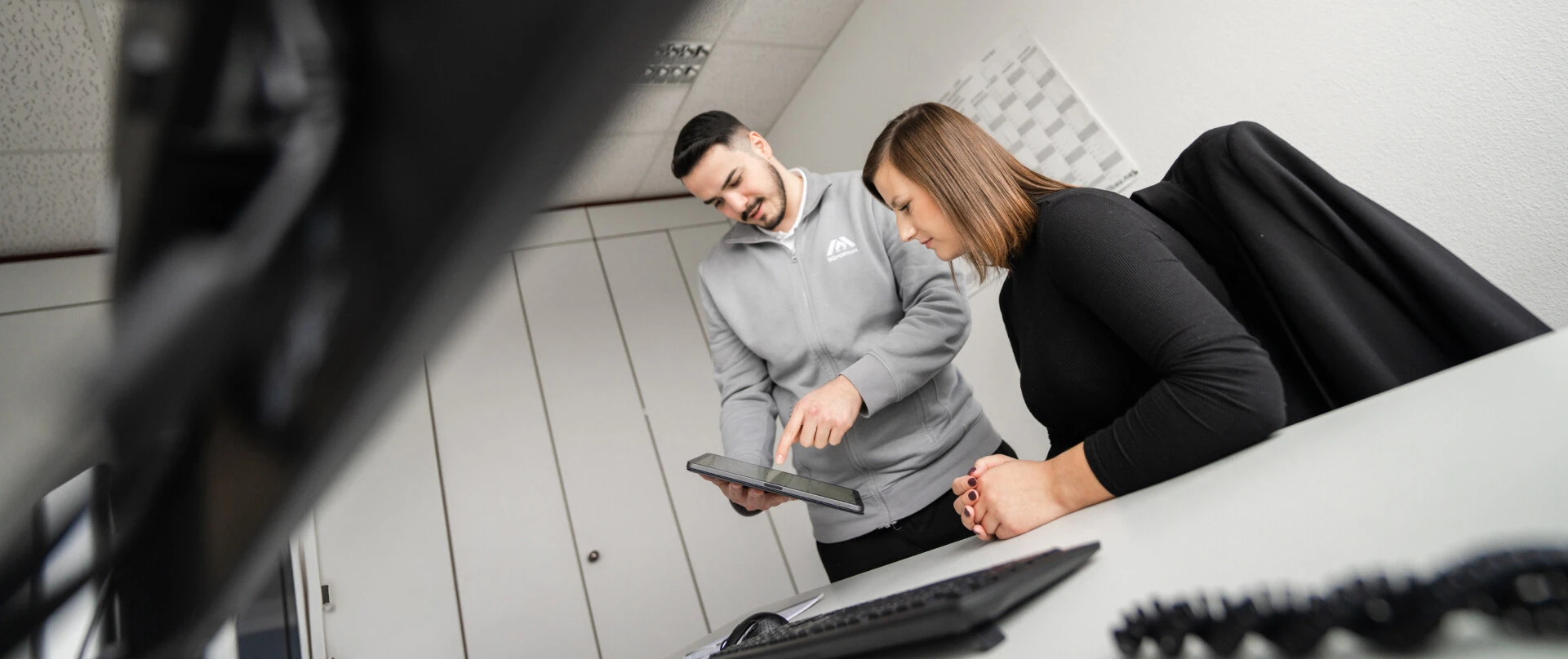 Deux personnes au bureau regardent une tablette. Un homme pointe l'écran tandis qu'une femme regarde attentivement.