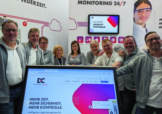 Photo de groupe des employés à un stand d'exposition, avec un écran d'ordinateur au premier plan affichant le site web de l'entreprise DÜPERTHAL connect.
