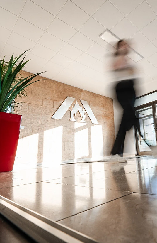 Une personne floue traverse un hall d'accueil moderne avec un aménagement végétal et un logo sur le mur.