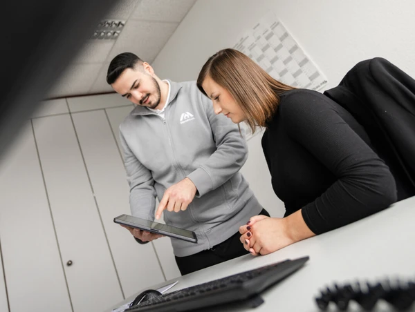 Deux personnes au bureau regardent une tablette. Un homme pointe l'écran tandis qu'une femme regarde attentivement.