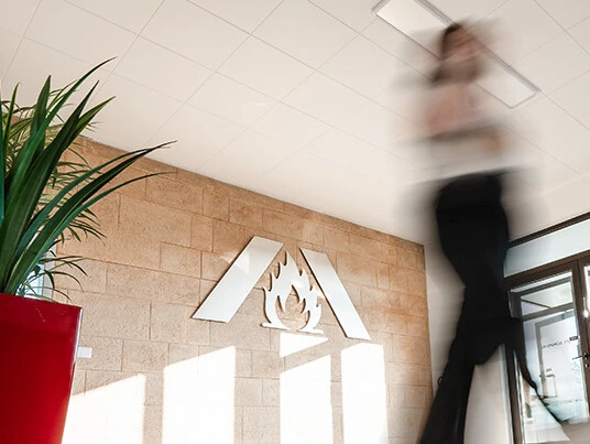 Une personne floue traverse un hall d'accueil moderne avec un aménagement végétal et un logo sur le mur.